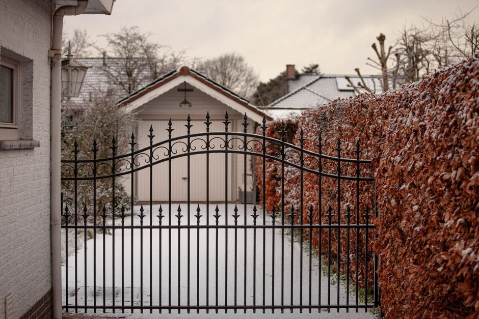 A serene snowy courtyard featuring a decorative iron gate and surrounding hedges in winter.